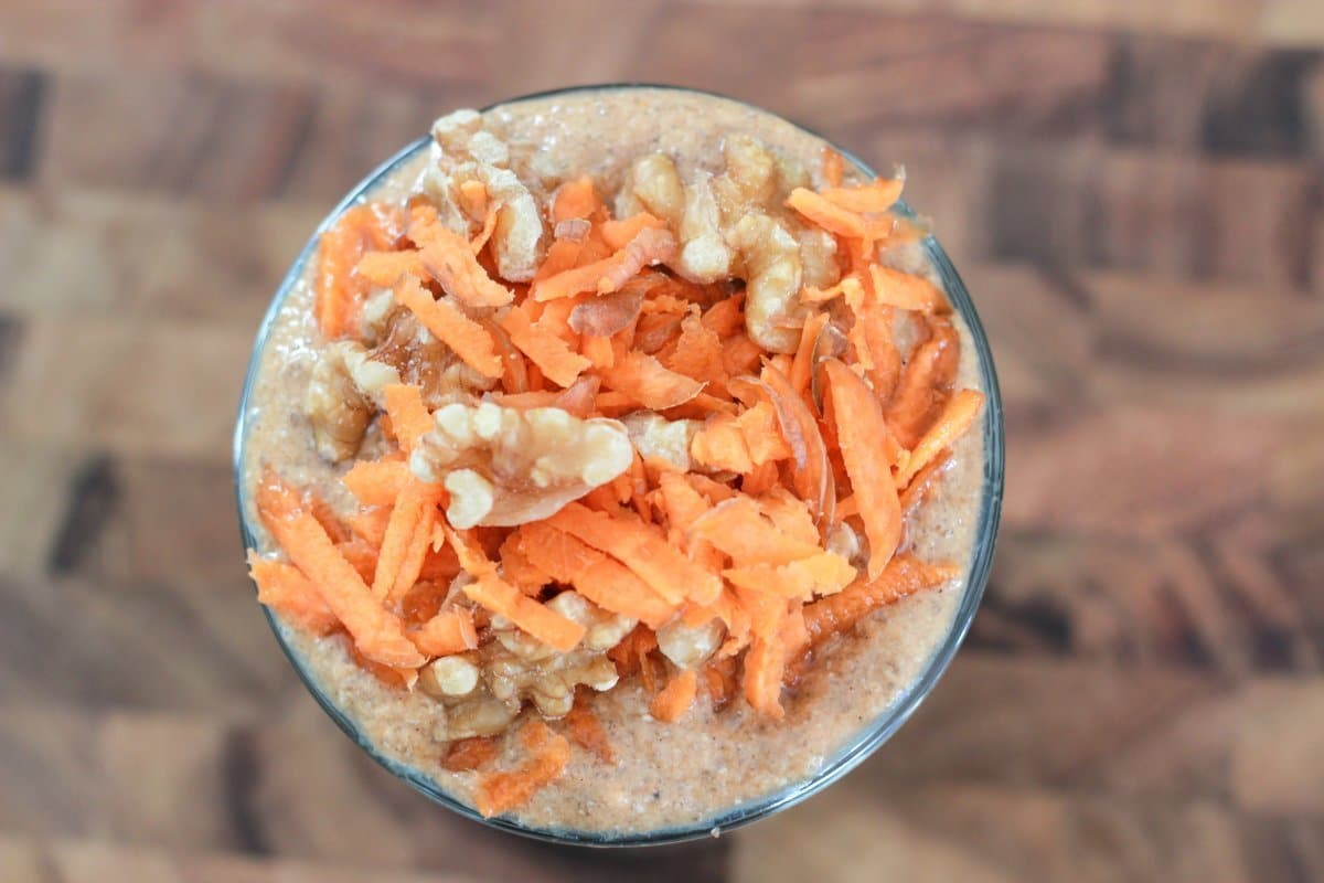 Carrot cake smoothie in a glass topped with shredded carrot and walnuts.