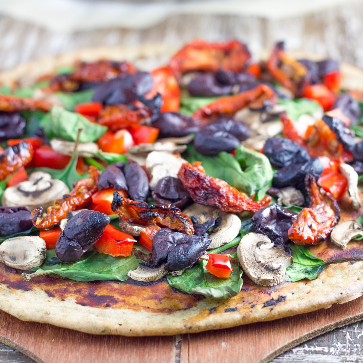 Pizza is topped with olives, sundried tomatoes, baby spinach and mushrooms. 