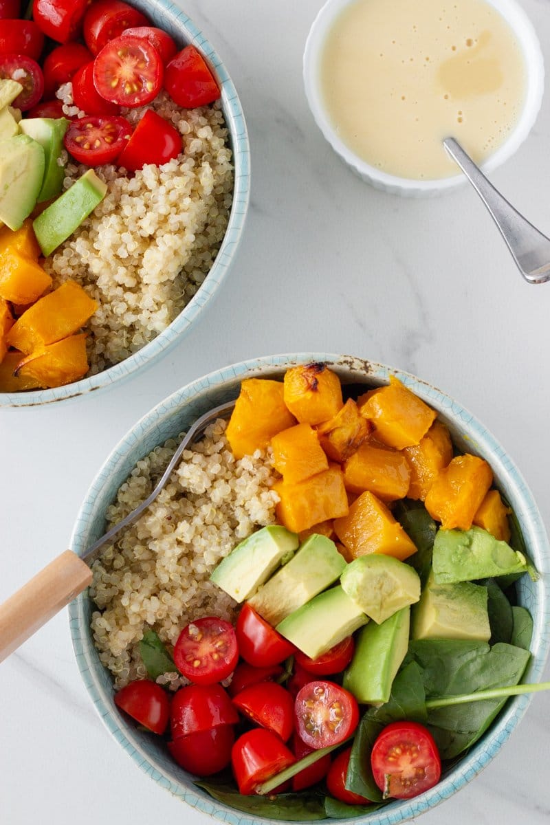 Two bowls of summer quinoa salad with the dressing next to it.