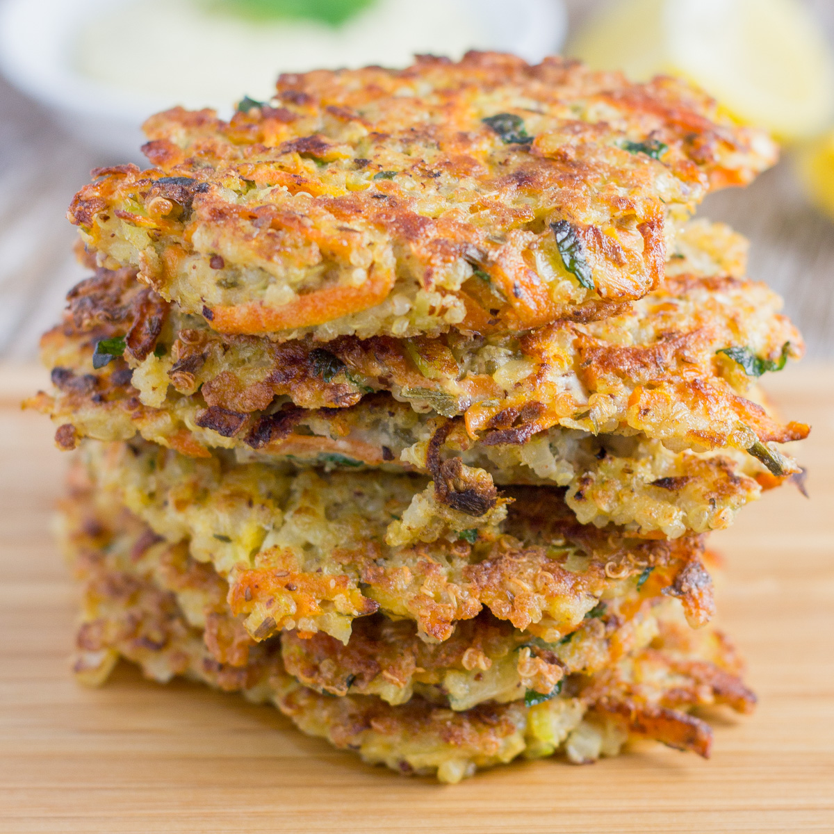 stack of quinoa fritters on a board with healthy garlic aioli in the background and lemon wedges