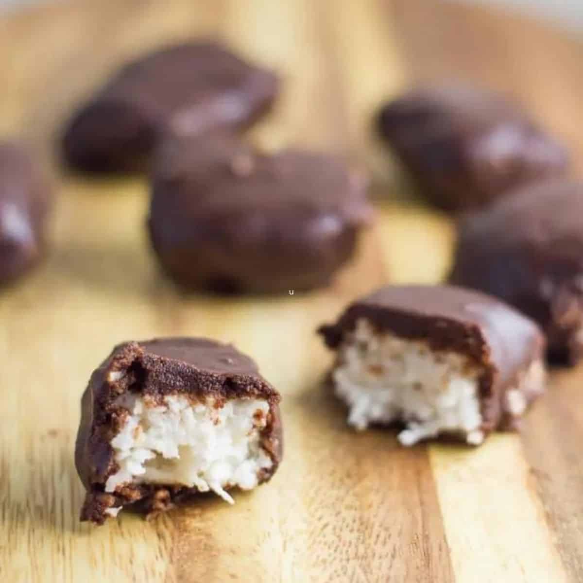 Coconut chocolate bars on a wooden board, with one cut in half showing the coconut mixture.