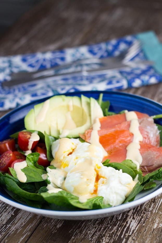 Breakfast Salad bowl with poached egg with hollandaise sauce, avocado, salmon, cherry tomato and spinach.