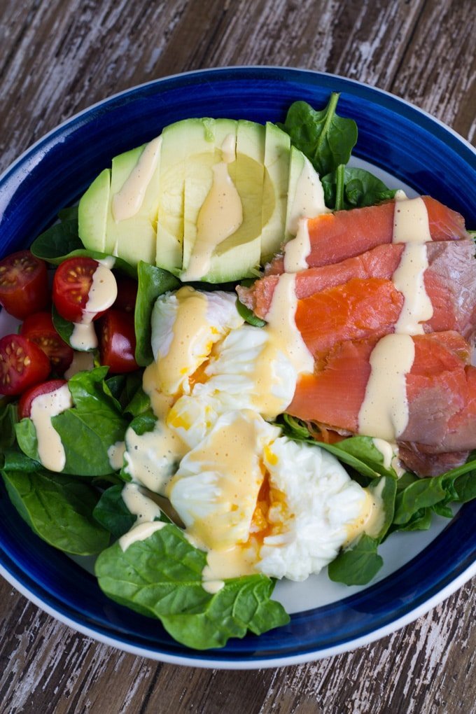 A bowl of salad with avocado, salmon, poached egg, tomatoes and baby spinach.