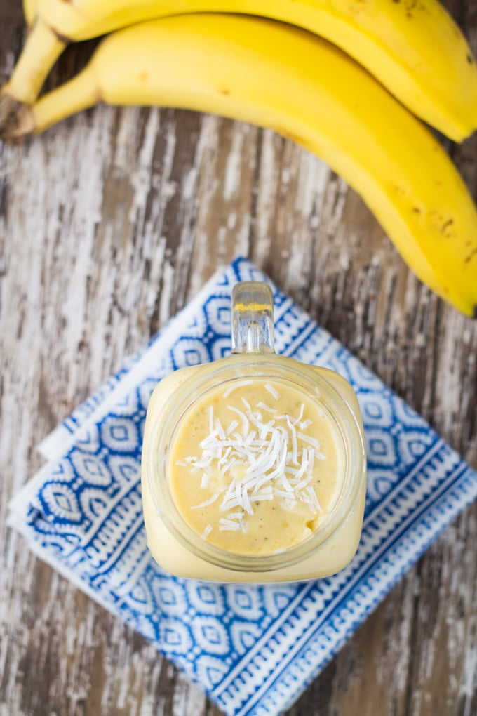 A glass of dairy free mango banana smoothie with some bananas near the glass.