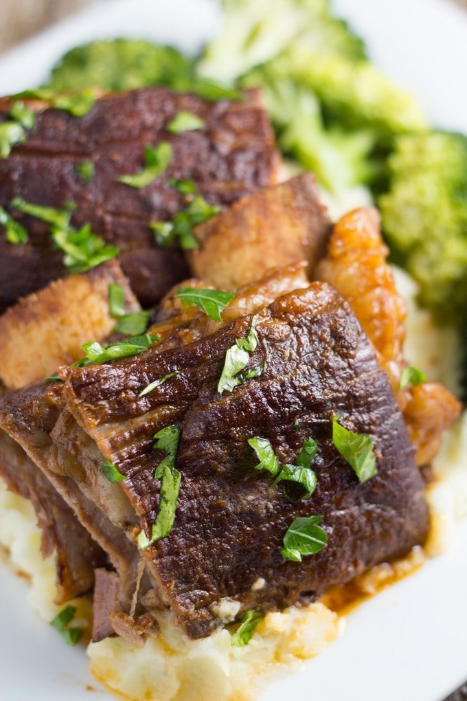 Slow cooker beef ribs on a plate with broccoli, potato mash and some parsley.