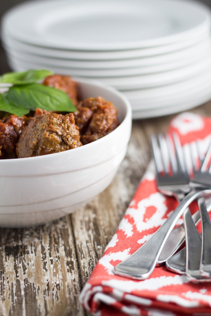 Bowl of meatballs on a table with plates and cutlery.