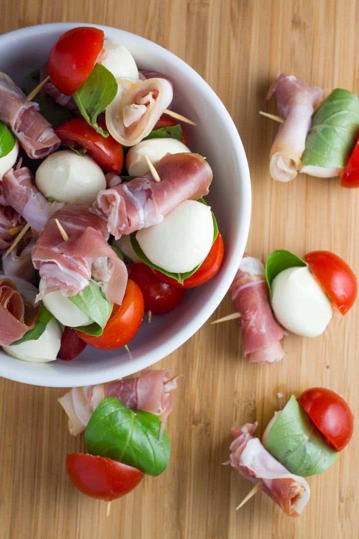 A bowl and board filled with the booconcini prosciutto skewers. 