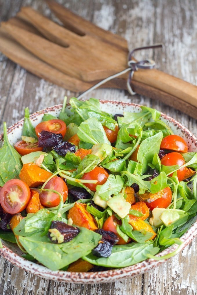 Bowl of roasted pumpkin and beetroot salad on a table with salad servers.