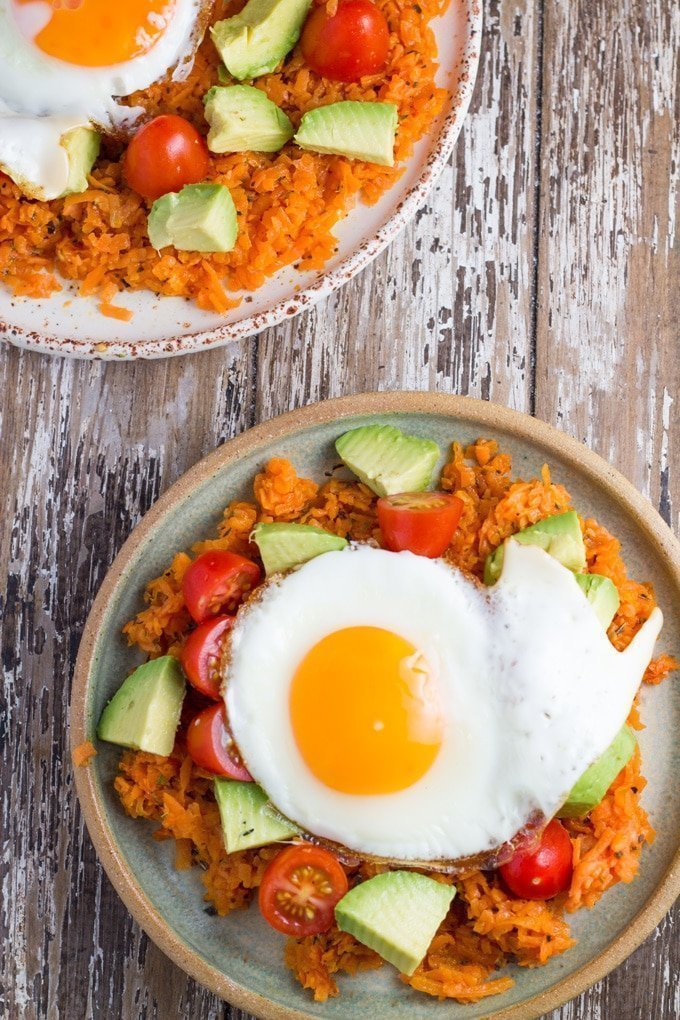 Plate of sweet potato breakfast has topped with tomato, avocado and a fried egg.