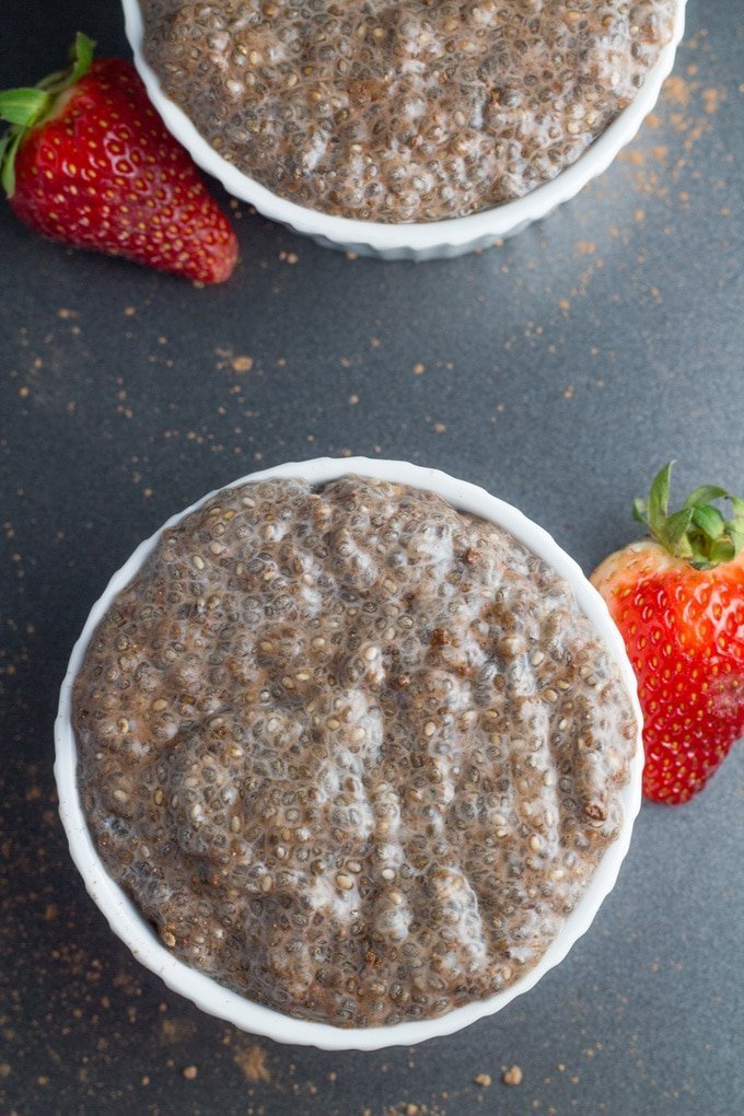 Chocolate Chia Pudding on a black plate with a strawberry next to it.