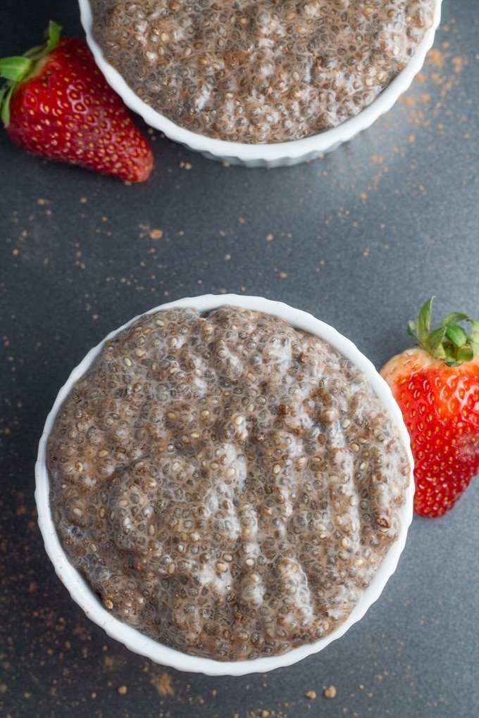 two chocolate chia puddings on black board with strawberries.