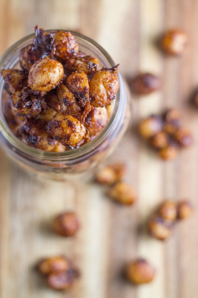 A jar of cinnamon macadamias with some of the nuts on a board.