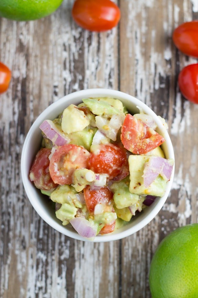 Bowl of chunky guacamole with some limes and cherry tomatoes surrounding the bowl