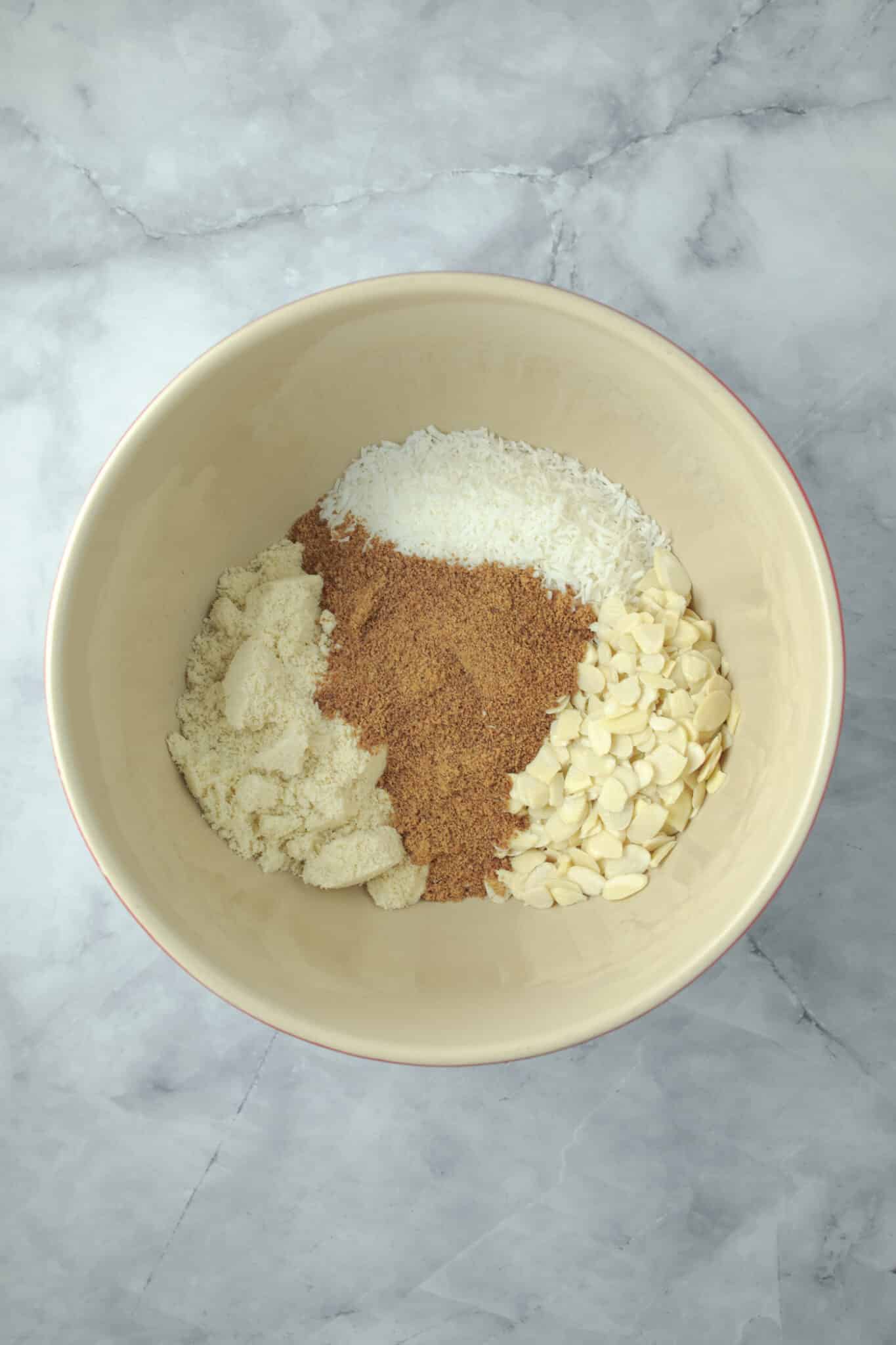 photo of the almond meal, shredded coconut, flaked almonds and coconut sugar added to a large mixing bowl