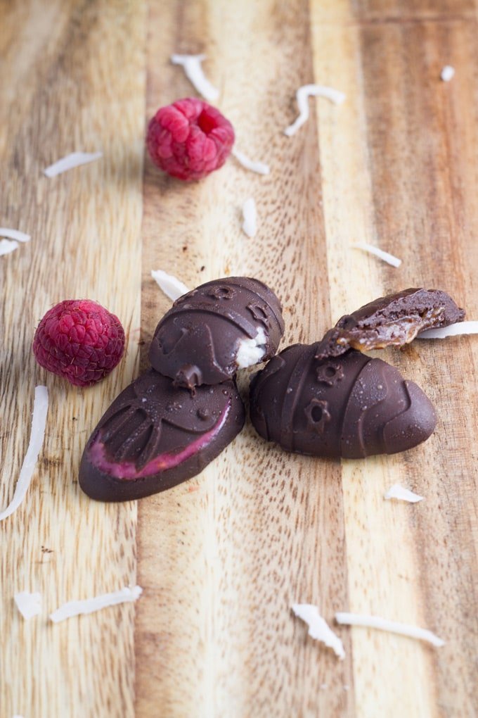 Three healthy easter chocolates on a board with some shredded coconut and fresh raspberries.