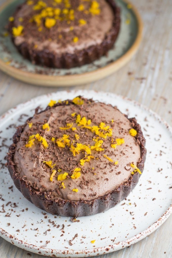 Two chocolate orange tarts on plates topped with shaved lemon rind.