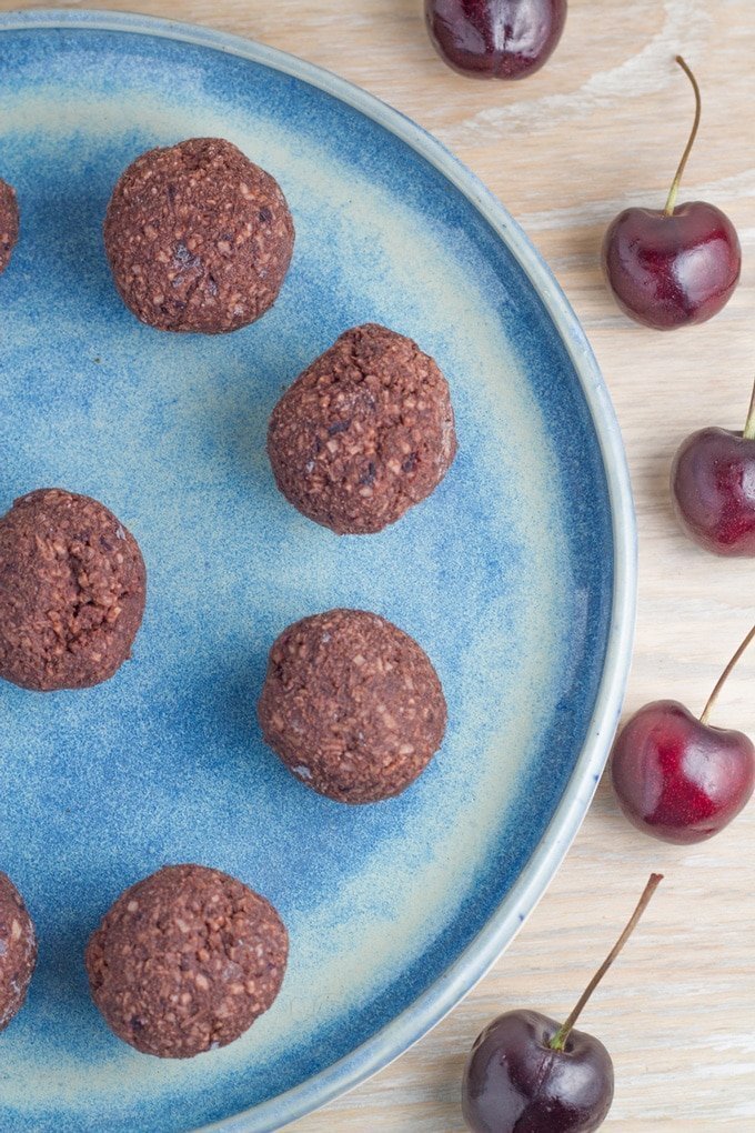 A plate of chocolate cherry balls with some fresh cherries.
