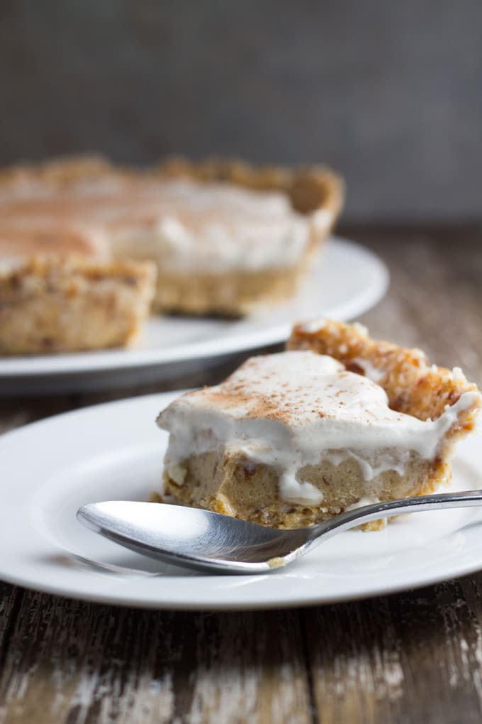 Slice of vegan banoffee pie on a plate with the rest of the pie in the background.