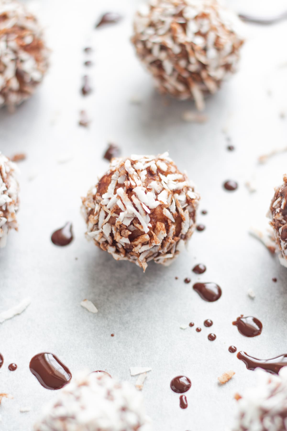 The bliss balls on baking paper with drizzled chocolate and coconut flakes.