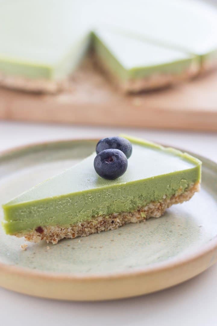 Slice of raw matcha cheesecake on a plate with the rest the cheesecake behind it.