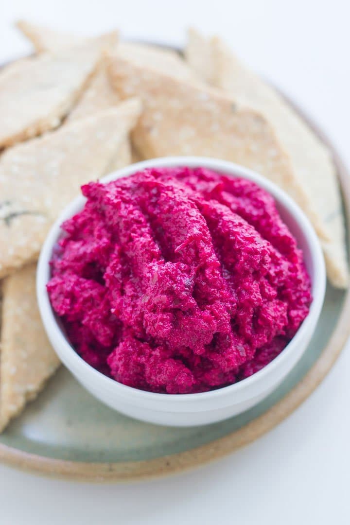 A bowl of beetroot dip with some crackers on a plate.