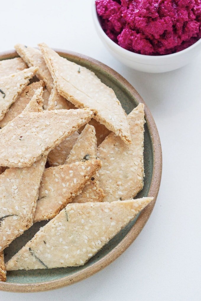Rosemary sesame seeds crackers on a plate with a bowl of beetroot macadamia dip.