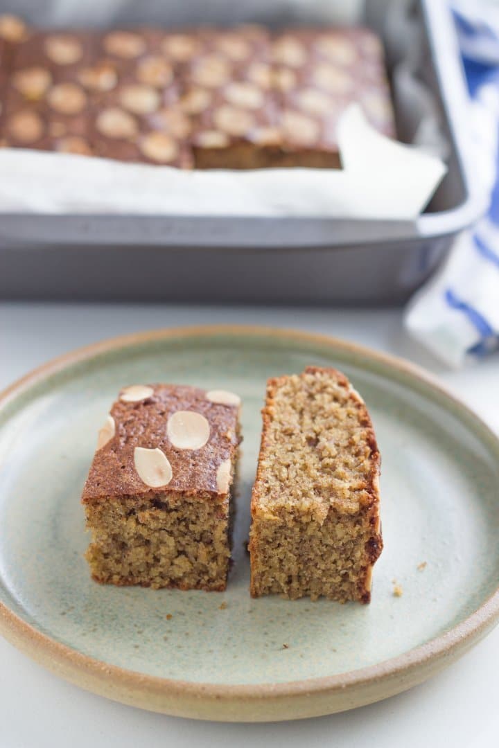 Two pieces of flourless Italian almond lemon cake on a plate with more of cake in the background.