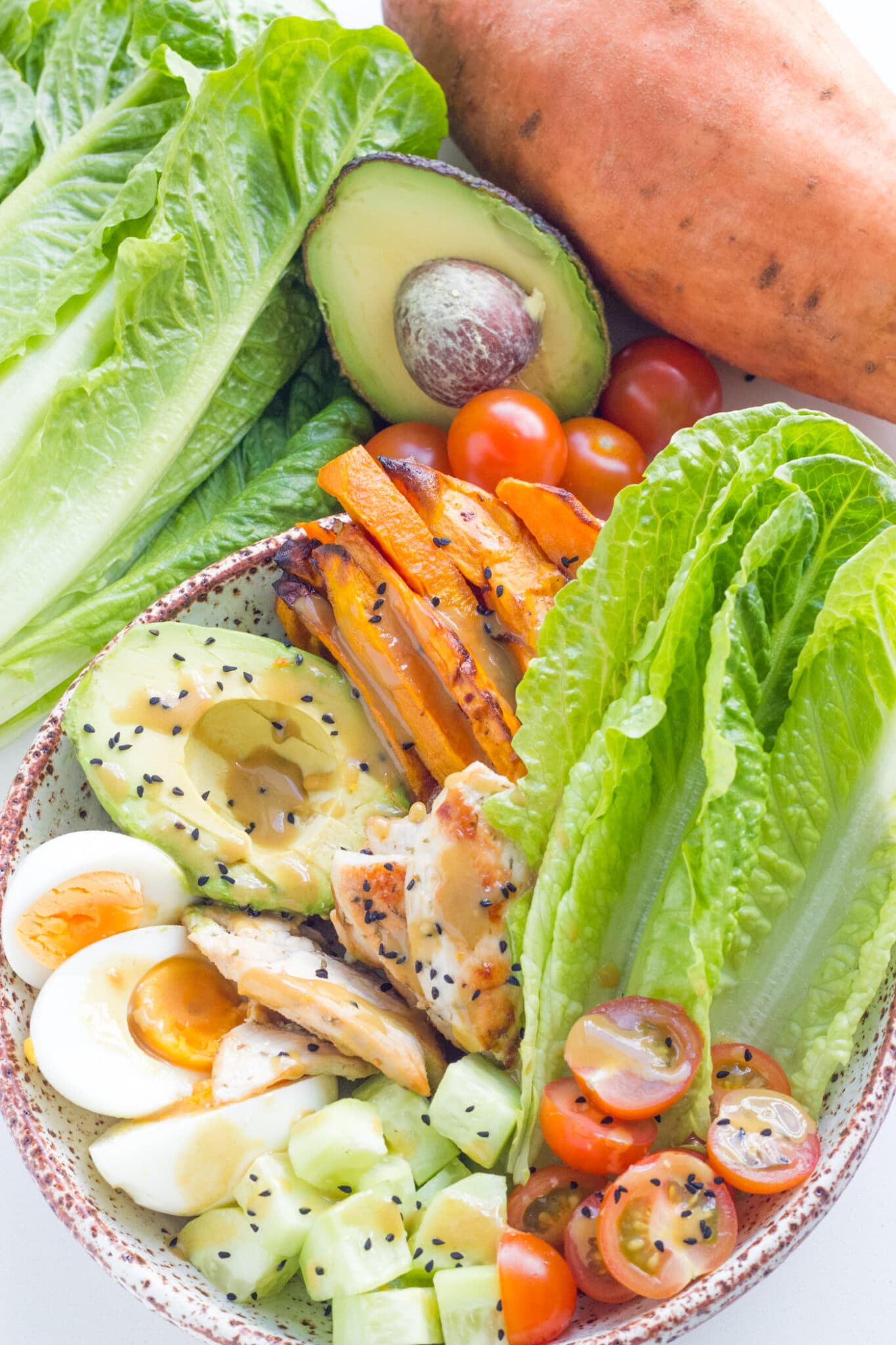 The salad with dressing on top, surrounded by the ingredients needed to make this meal.