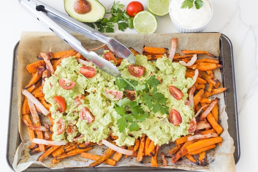 Tray of sweet potato fries topped with guacamole and bacon.