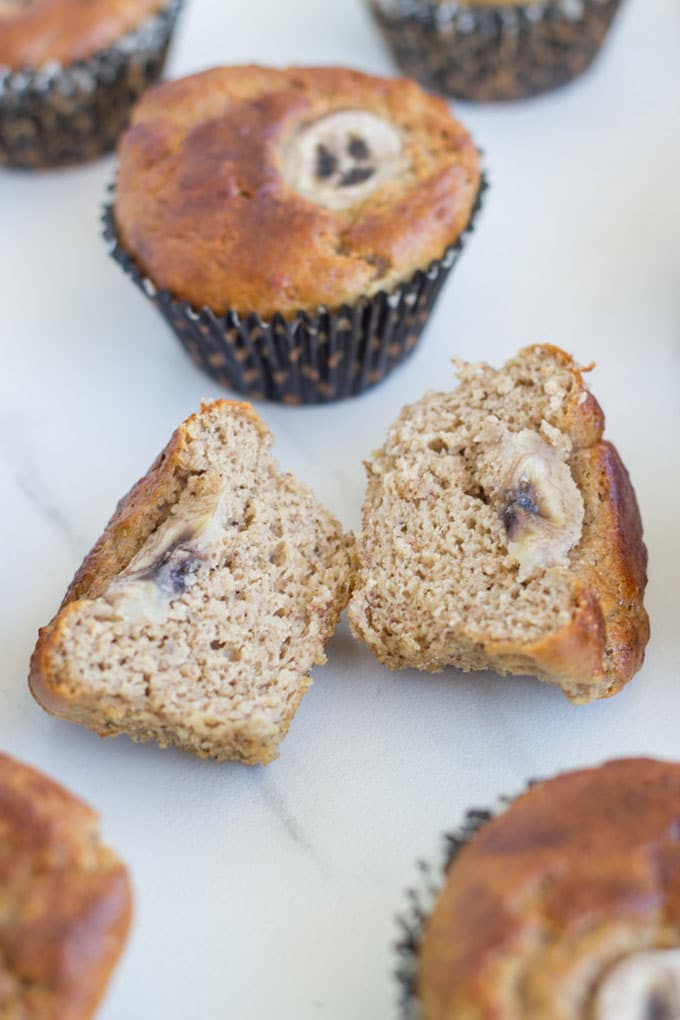 a banana muffin cut in half with a few surrounding it. 