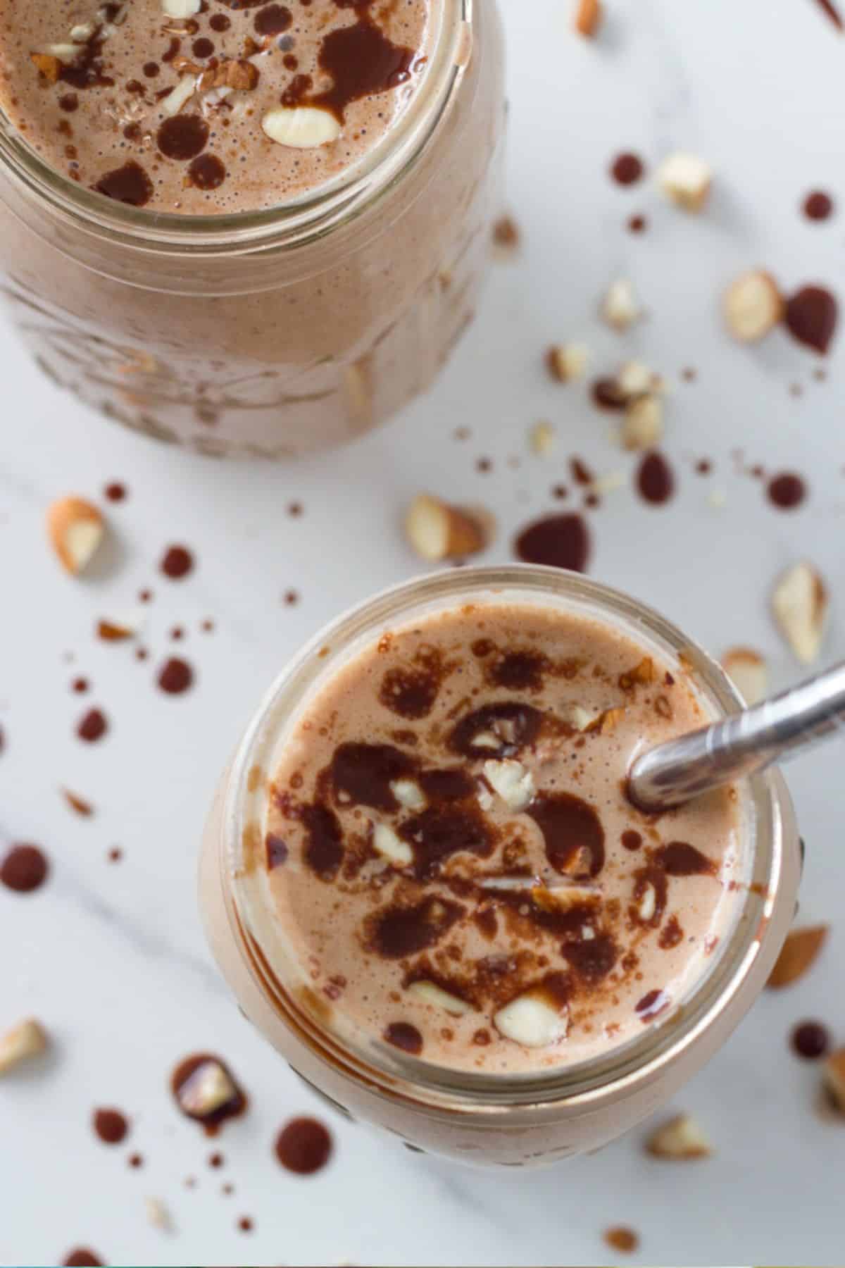 Chocolate smoothie in two glasses with some nuts and chocolate sauce swirled over the top.