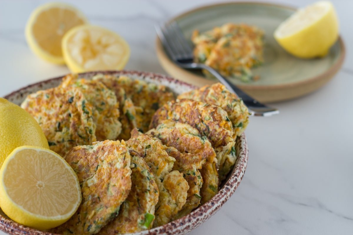 Bowl of fritters with a plate and some lemon behind it. 