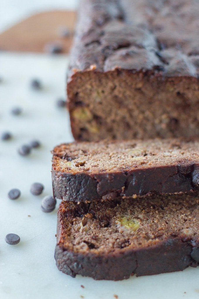 Chocolate banana bread on a ceramic/wooden board with a few slices cut in front.