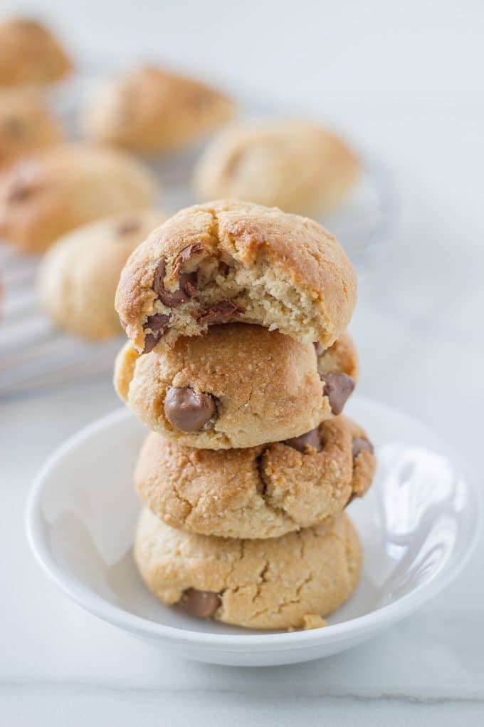 four gluten free chocolate chip cookies stacked on top of each other with more cookies in the background on a wire rack.