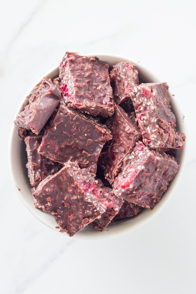 A bowl of raspberry coconut rough pieces in a white bowl on a white background.