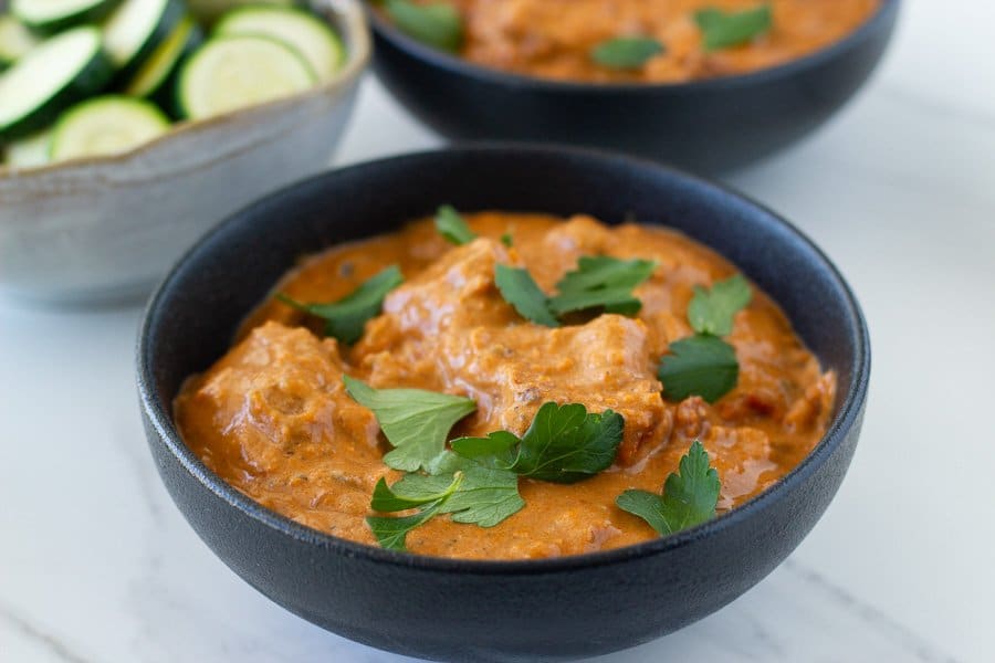 a bowl of butter chicken and one in the background that were made in an instant pot plus a bowl of cooked zucchini