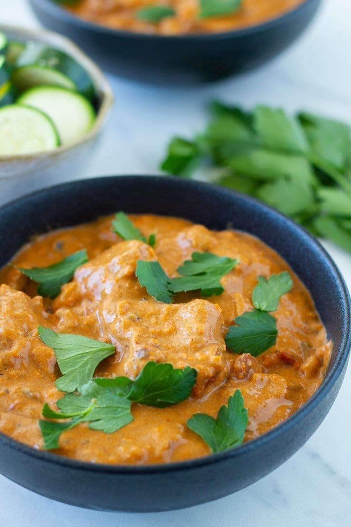 a bowl of butter chicken and one in the background that were made in an instant pot plus a bowl of cooked zucchini and some fresh herbs