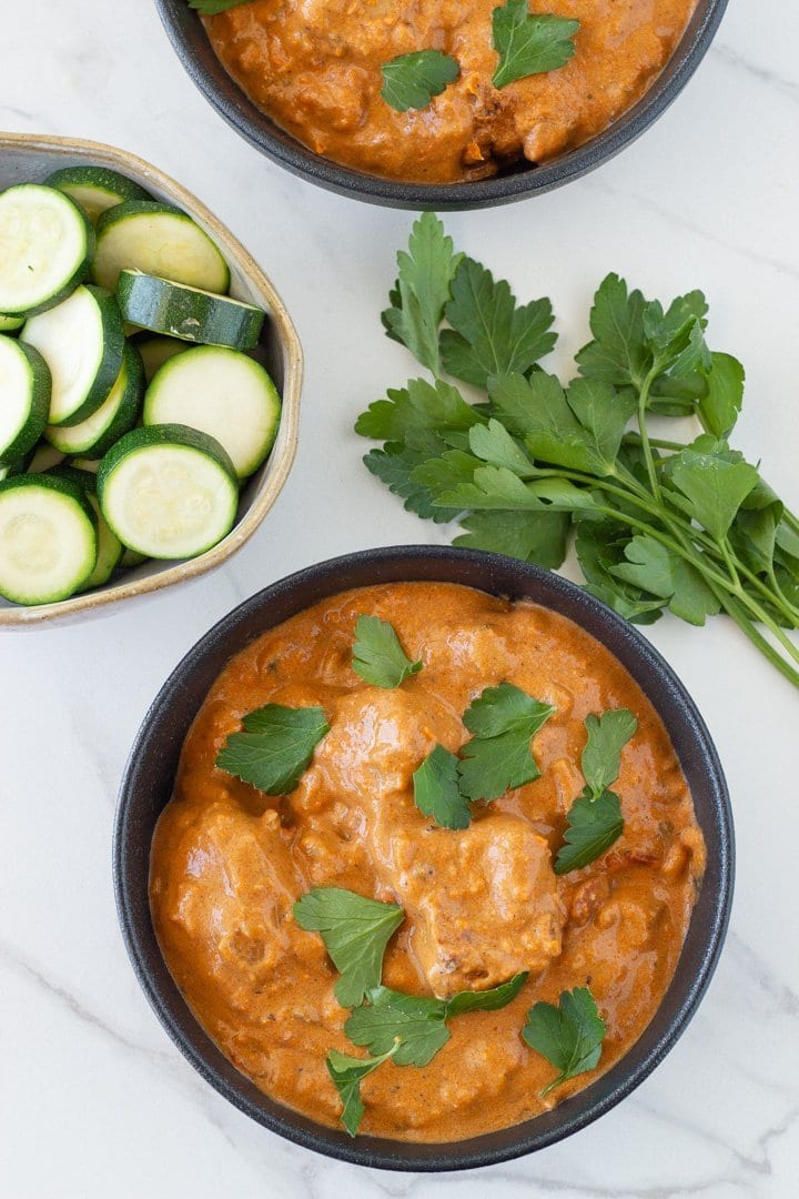 two bowls of butter chicken that were made in an instant pot plus a bowl of cooked zucchini and some fresh herbs