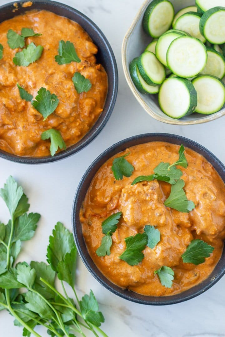 two bowls of butter chicken that were made in an instant pot plus a bowl of cooked zucchini and some fresh herbs