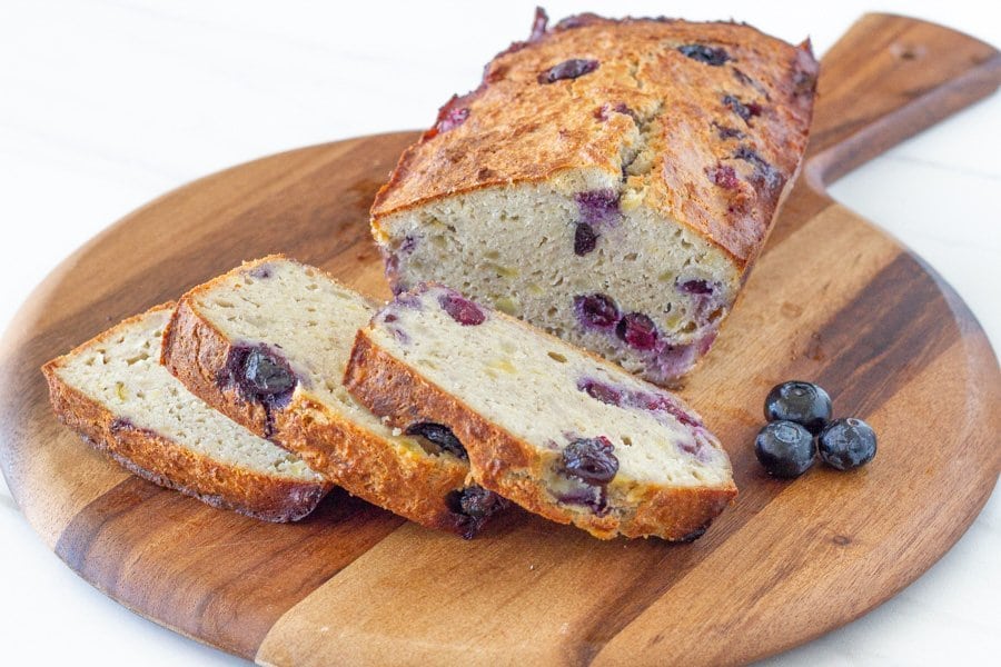 Slices of the banana bread in front of the rest of the loaf on a round wooden board.