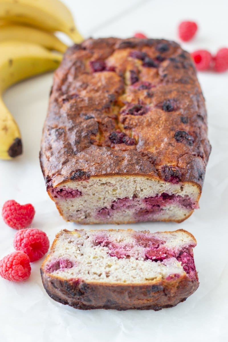 Loaf of healthy banana raspberry bread with bananas and raspberries surrounding it.