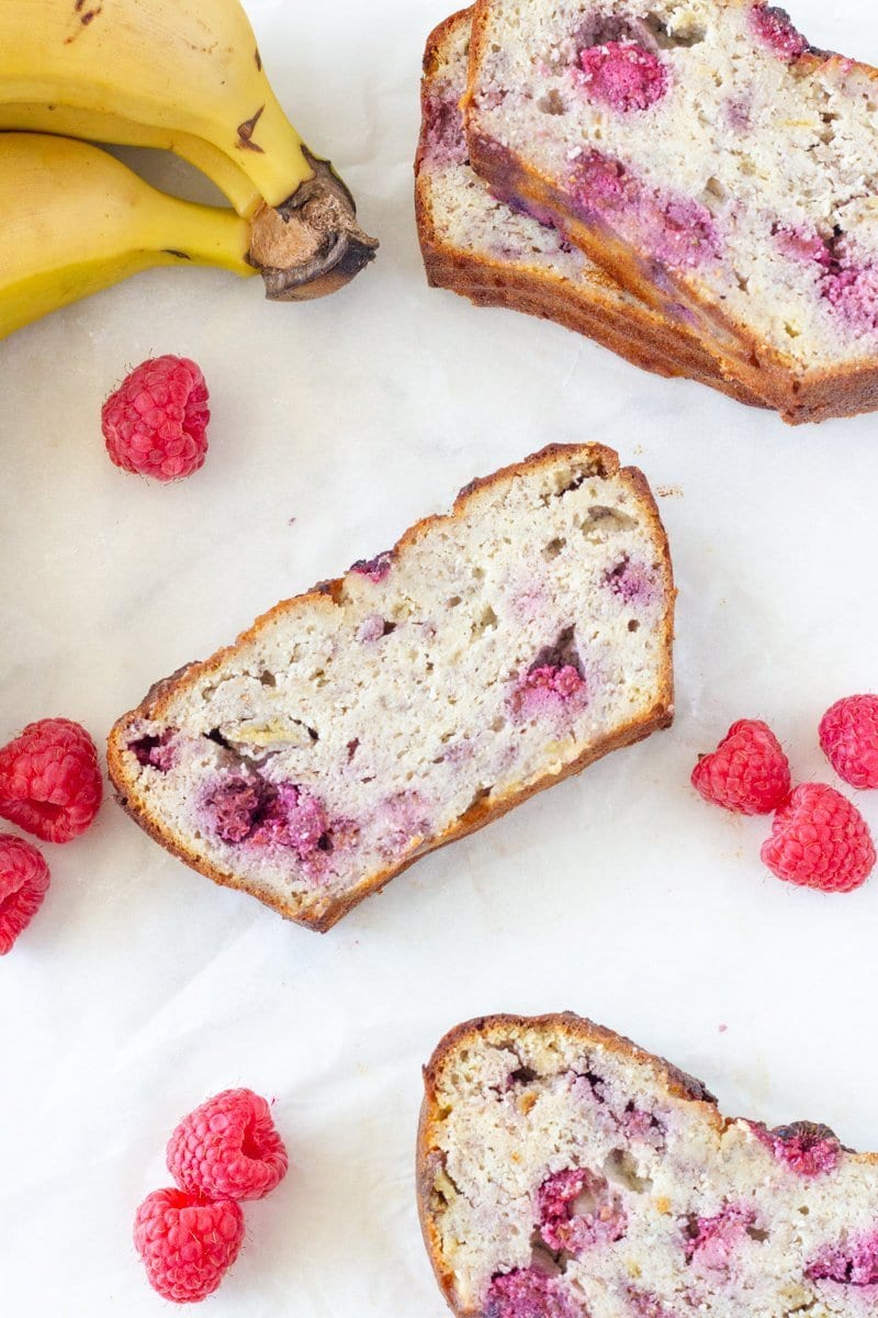 Sslices of the banana bread with raspberries and banana around them.