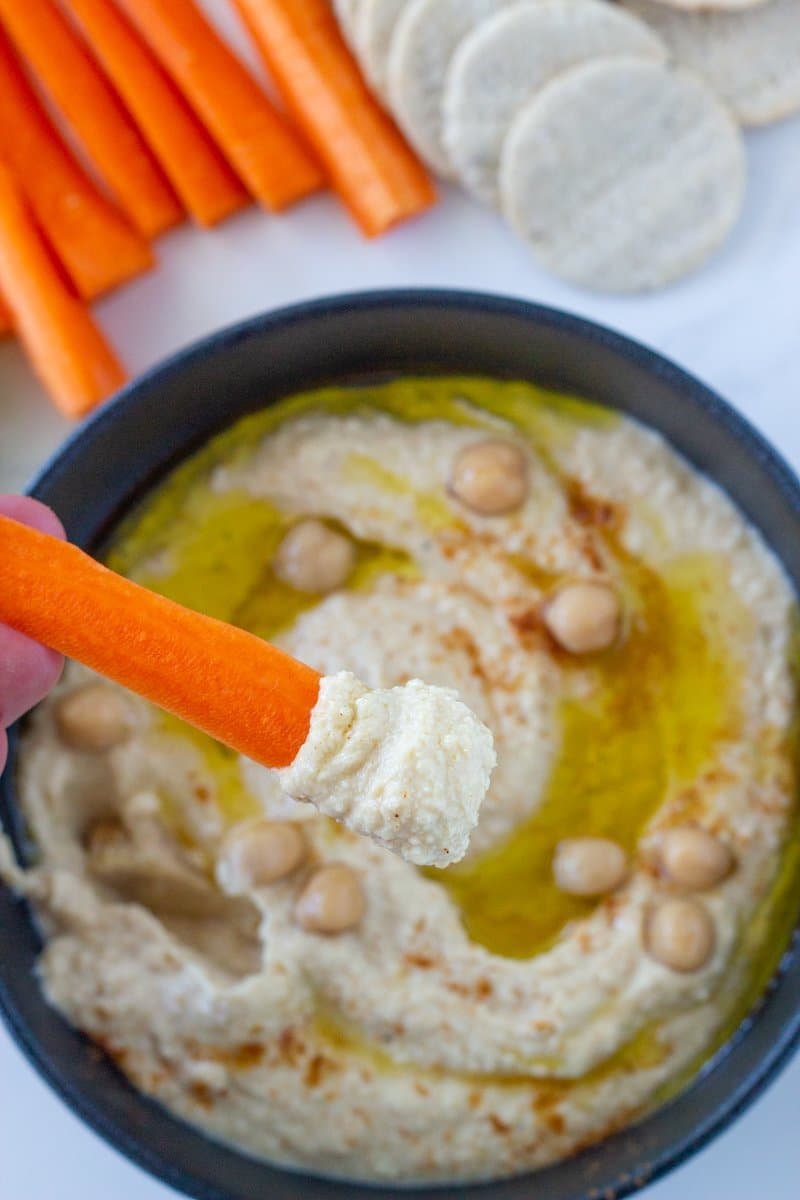carrot sick with hummus above the bowl of hummus