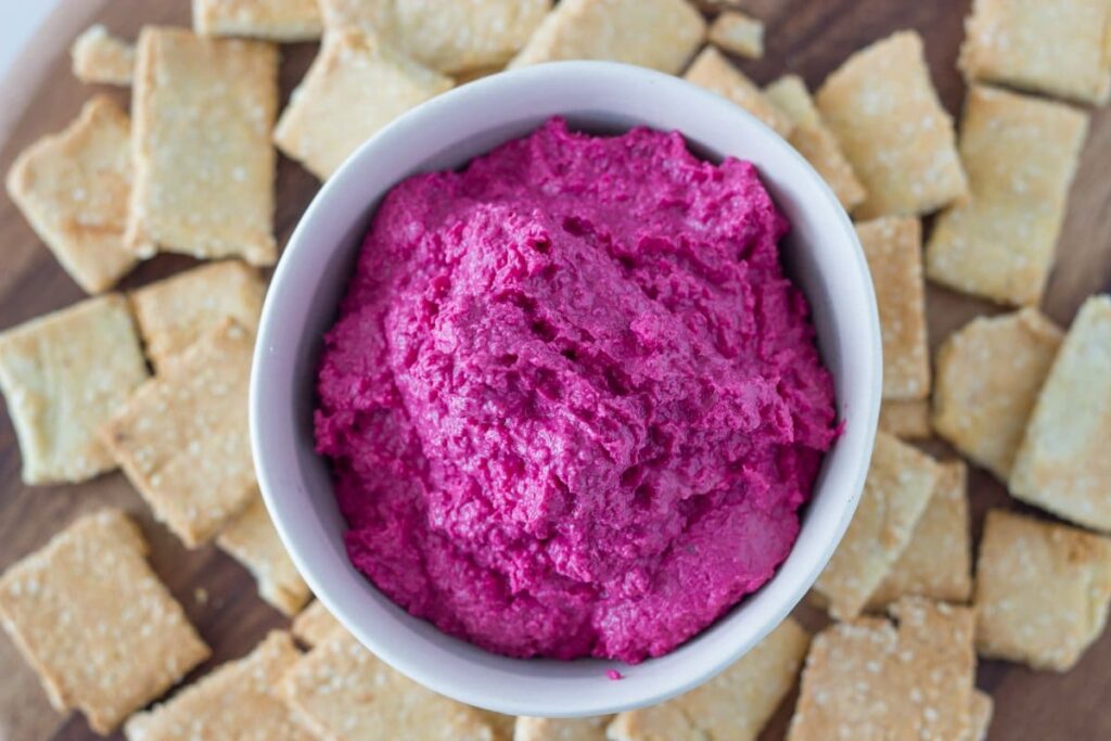 top down view of beetroot hummus in a bowl with homemade crackers around the bowl