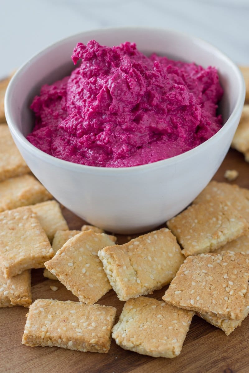 Beetroot hummus in a bowl with crackers in front of it.