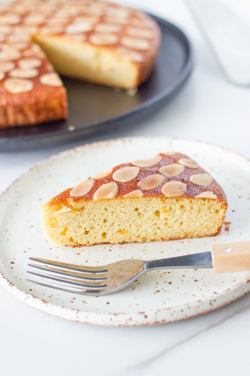 Slice of gluten free orange almond cake on a plate with the rest of the cake.