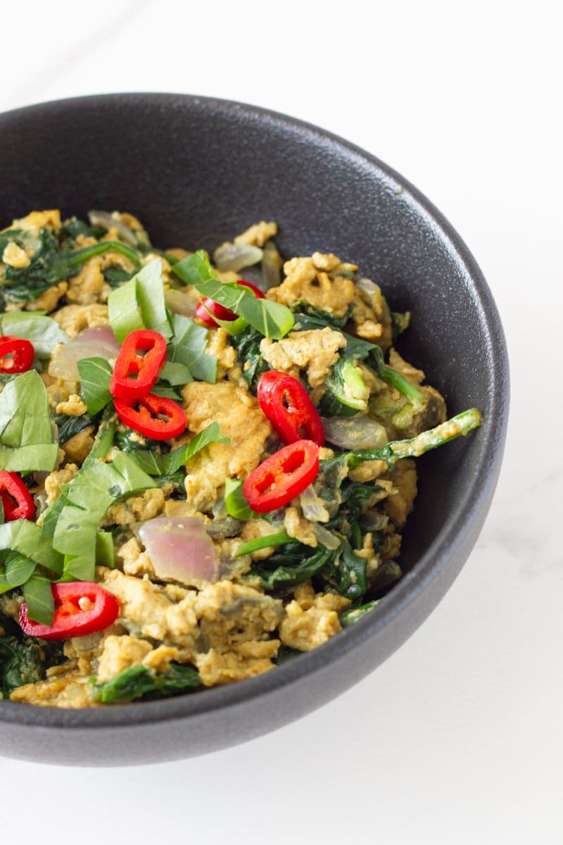 Breakfast bowl with scrambled eggs, spinach, onion, herbs and chili