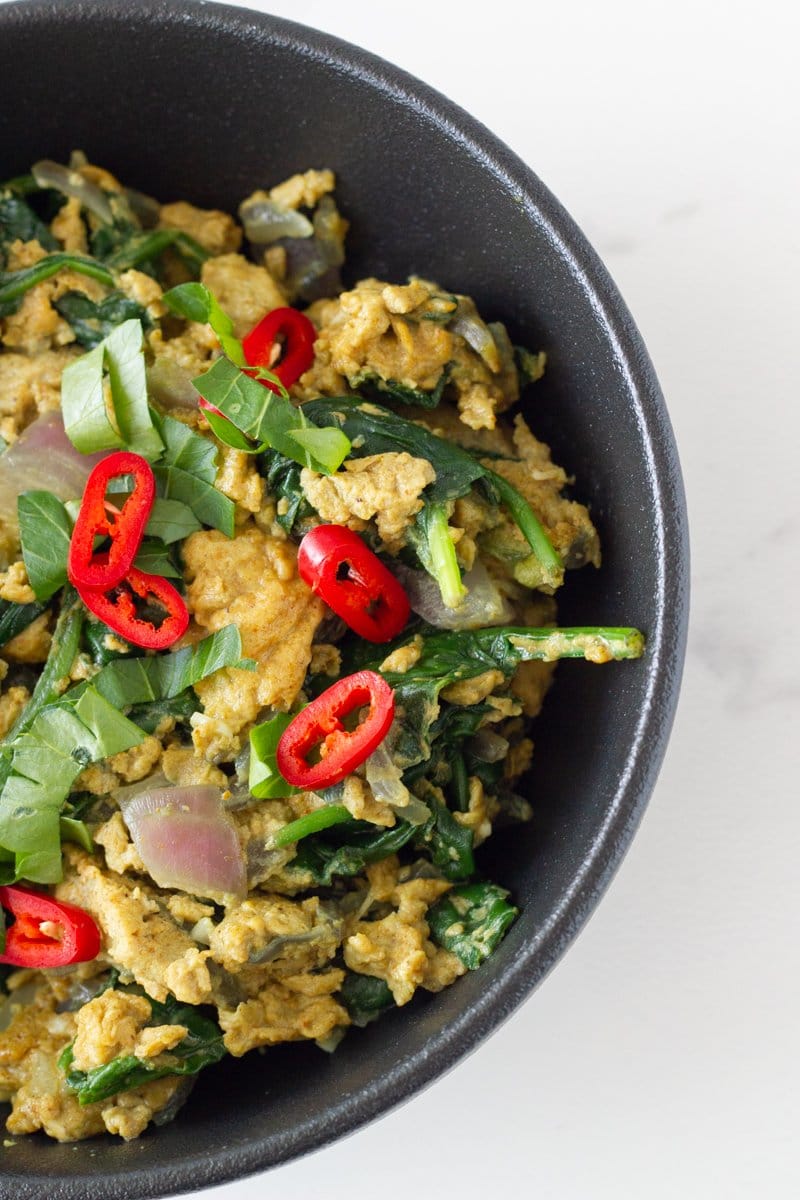 A bowl of curried scrambled eggs topped with fresh herbs and chili.