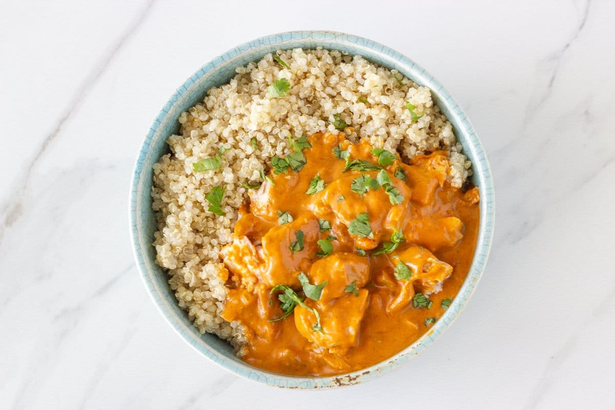 A blue bowl with chicken tikka marsala and quinoa topped with coriander.