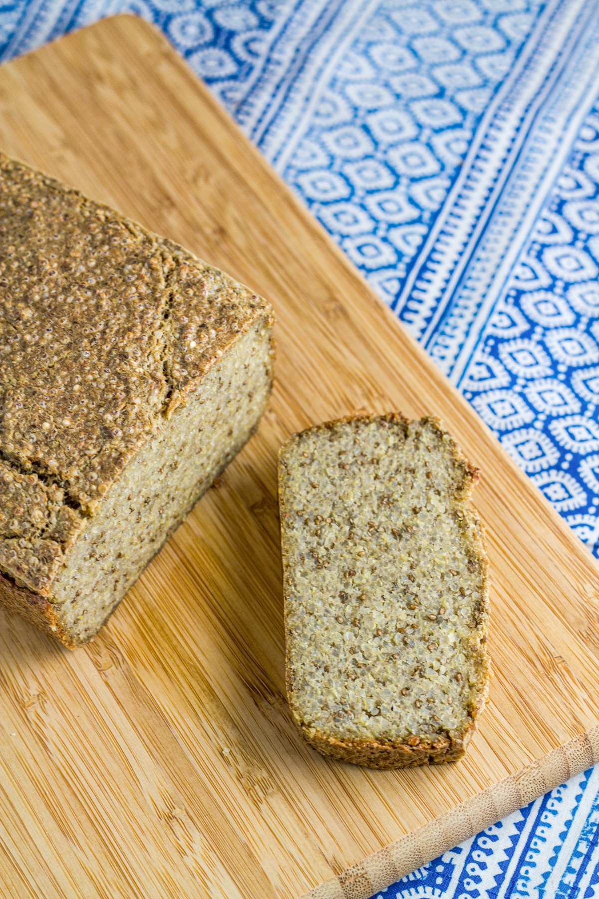 a slice of Quinoa & Chia Seed Bread with the rest of the loaf on a wooden board.l